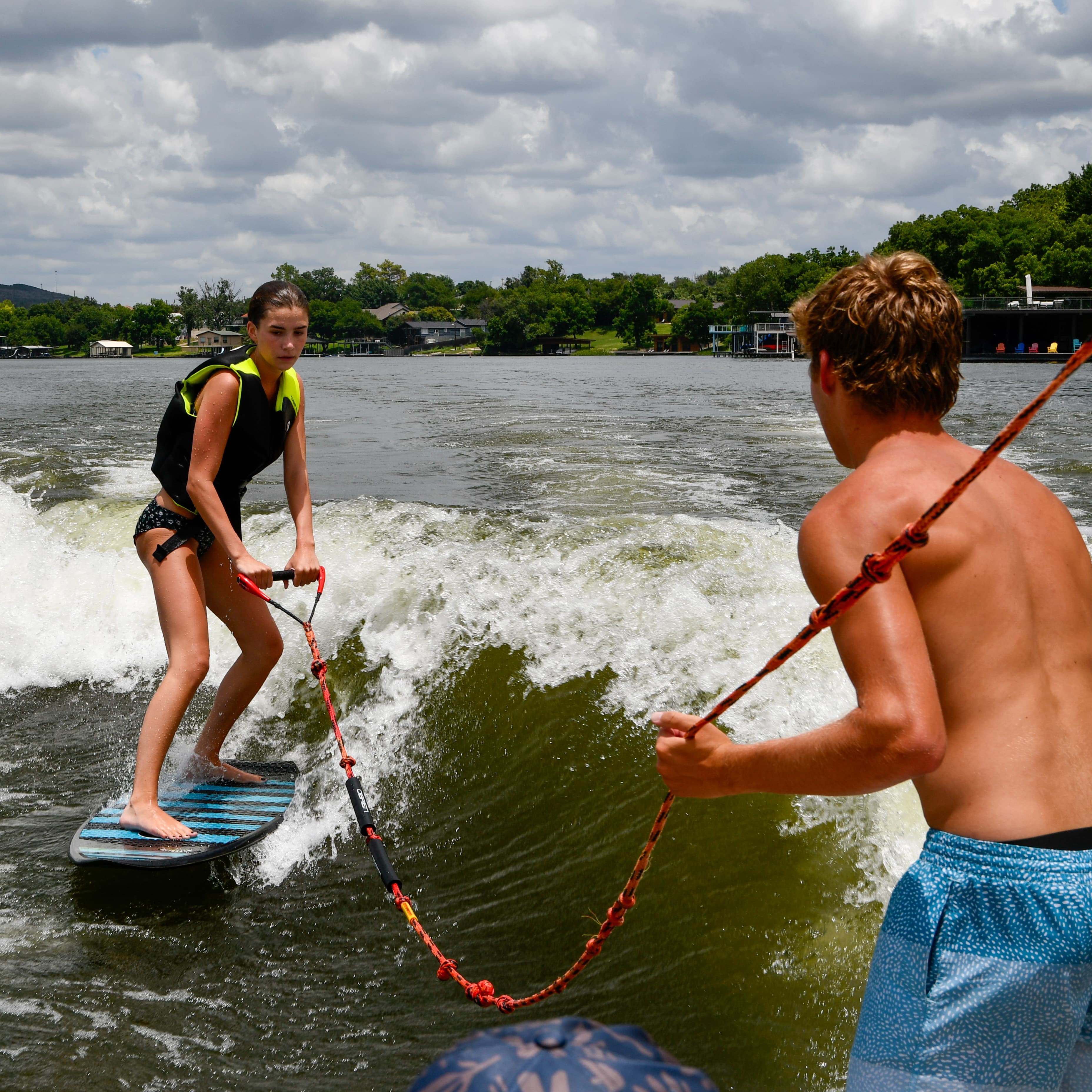 An instructor coaching a guest from the back of a wake boat during a wakesurf lesson on a Texas hill country lake.